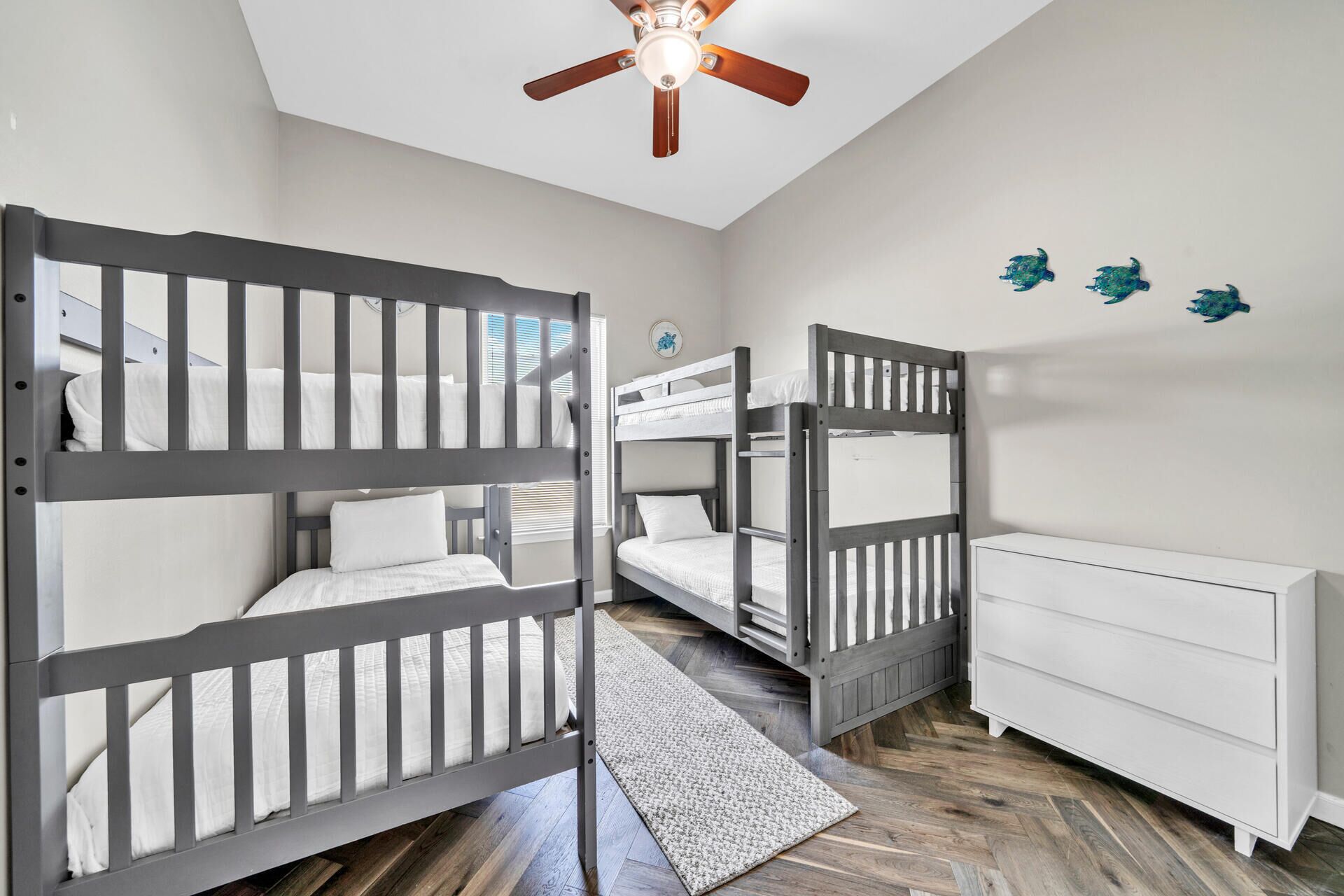 A room with two bunk beds, a white dresser, a ceiling fan, and a small rug.