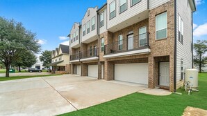 A multi-story apartment building with a brick facade, multiple garage doors, and a well-maintained lawn. - Beautiful 2 Bedroom Home Near Old Town Spring (Humble)