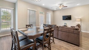 A modern living room with a dining area, a ceiling fan, and a flat-screen TV mounted on the wall. - Beautiful 2 Bedroom Home Near Old Town Spring (Humble)