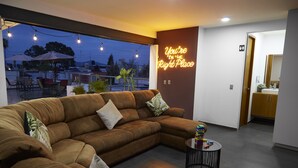A modern living room with a large sectional sofa, a small round coffee table, and a neon sign on the wall. - Casa Cheljo (Guadalajara)