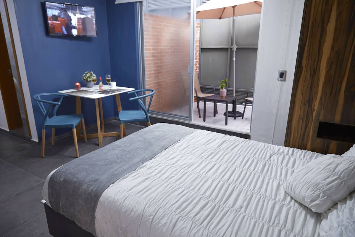 A hotel room with a bed, a desk with two chairs, a TV on the wall, and a sliding glass door leading to an outdoor area.