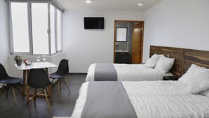 A hotel room with two beds, a desk with chairs, a TV, and a bathroom door. - Casa Cheljo (Guadalajara)