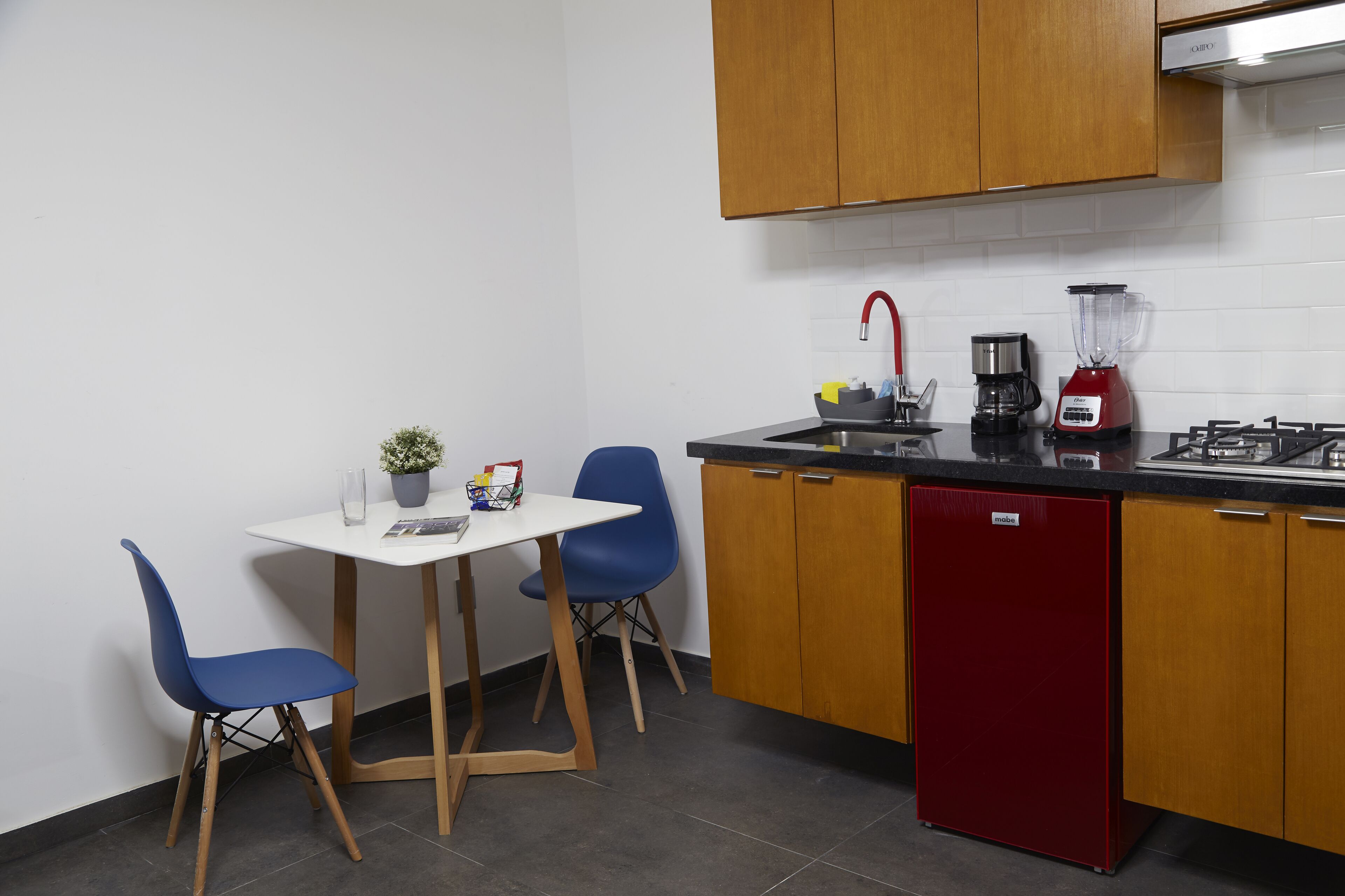 Une cuisine compacte avec des meubles en bois, un lave-vaisselle rouge, une machine à café et un mixeur posés sur le plan de travail.