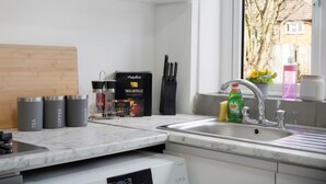 Una cocina moderna con encimera de mármol, lavavajillas integrado y ventana con vistas a árboles y una casa.