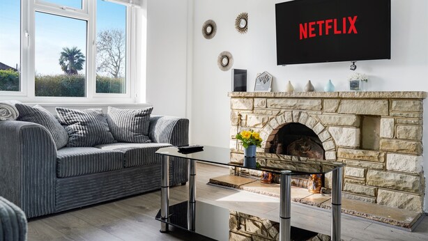 Una sala de estar moderna con una chimenea de piedra, un sofá, una mesa de centro y un televisor en la pared mostrando 