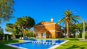 A house with a swimming pool, surrounded by well-maintained grass and palm trees.