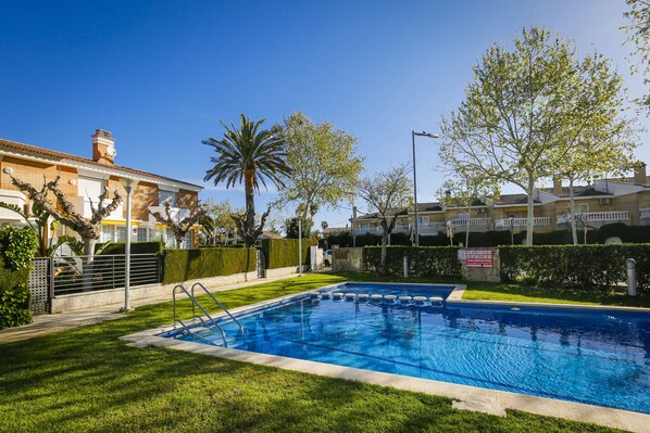 A swimming pool with a metal ladder, surrounded by well-maintained grass and trees.