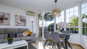 A modern living room with a grey sofa, a glass dining table, and artwork on the walls.