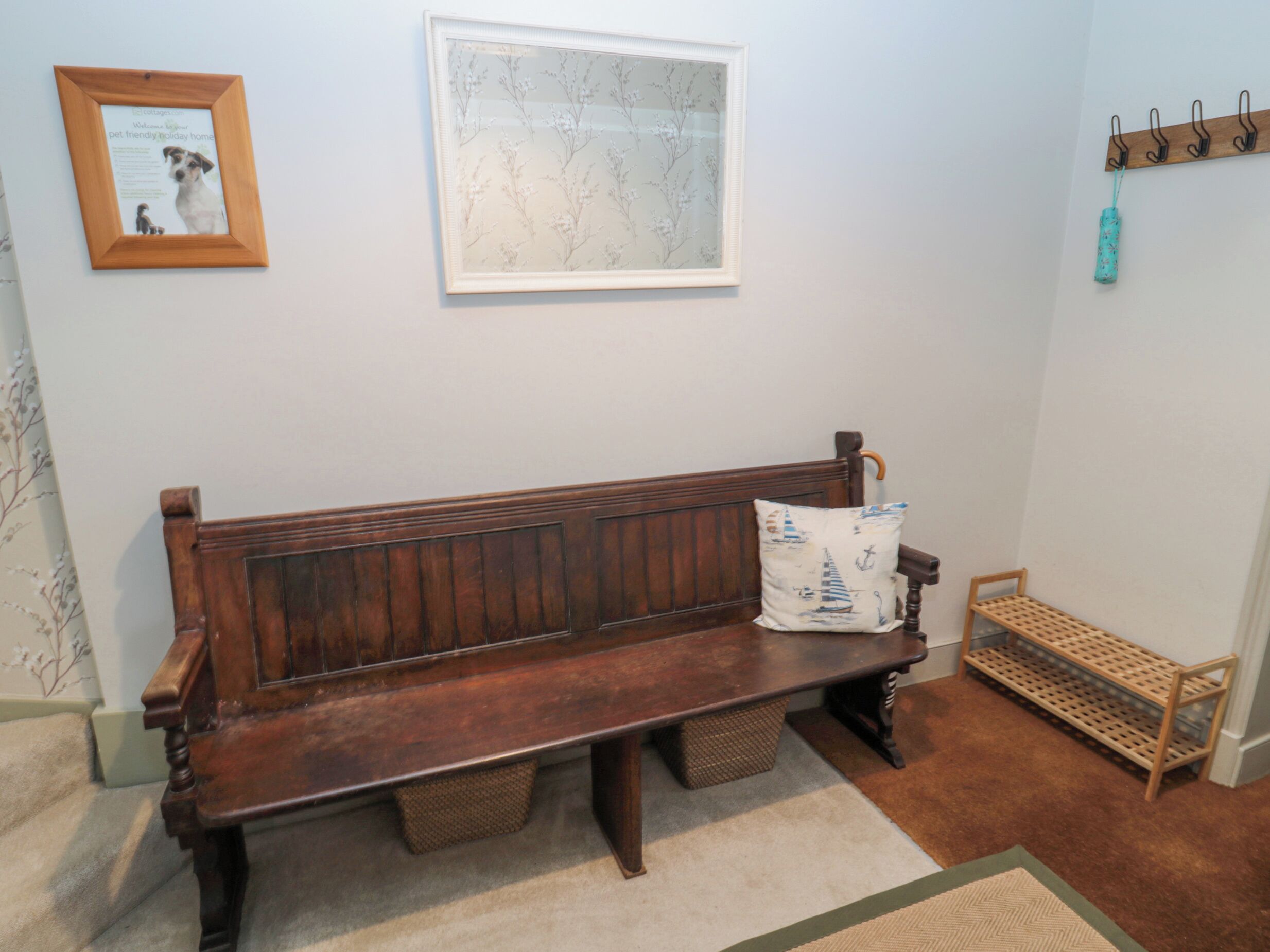Un banc en bois avec des paniers de rangement en dessous, un panneau d’accueil encadré, une carte accrochée au mur et un porte-manteau avec un manteau et un sac.