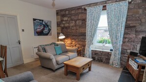 Ein gemütliches Wohnzimmer mit Steinwand, einer Couch, einem Holztisch und einem Fernseher.