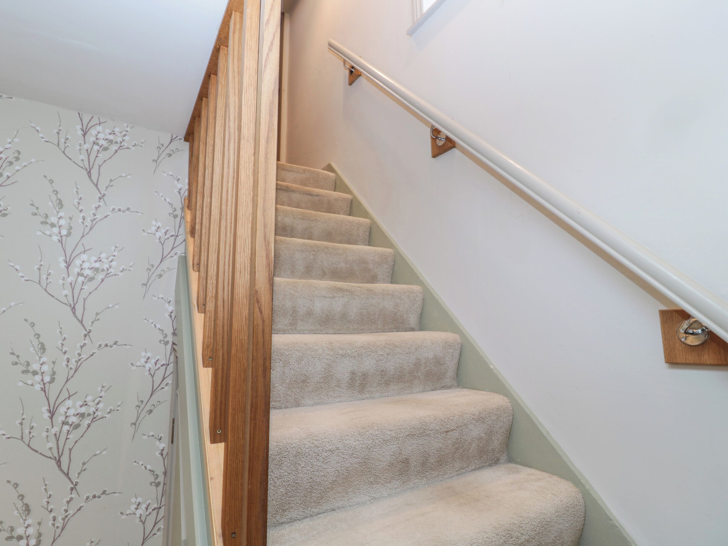 A carpeted staircase with wooden handrails and a wall with floral wallpaper.
