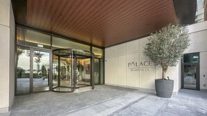 A modern building entrance with a revolving door, a large potted tree, and a sign reading "PALACE RESIDENCES". - Palace Waterfront Living Dubai Creek  (Dubai)