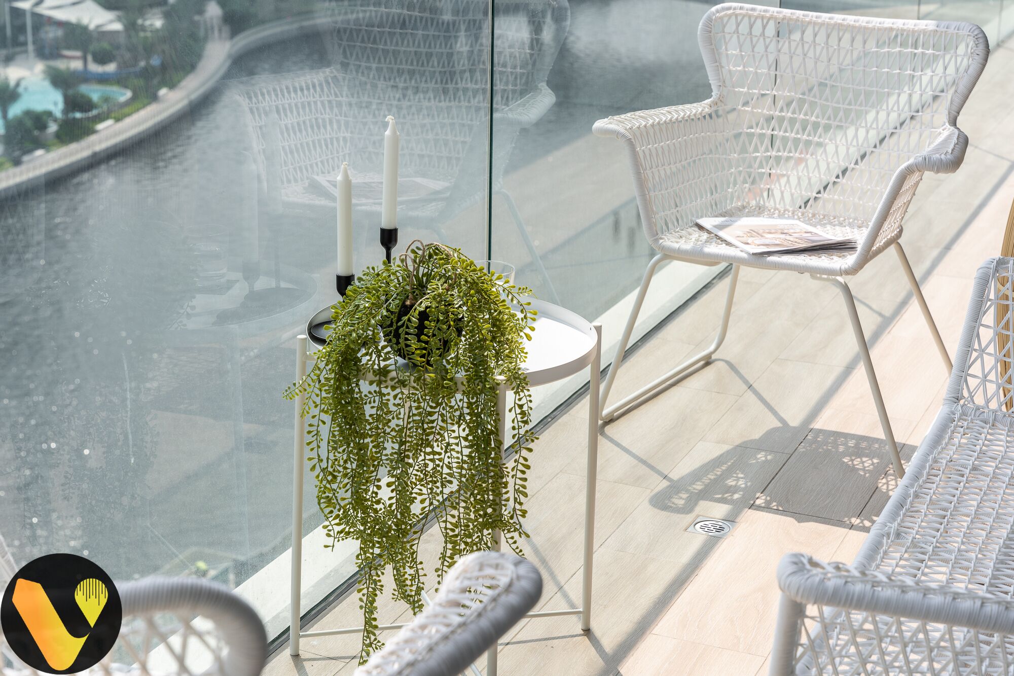Un balcon avec des fauteuils en osier peints en blanc, une petite table sur laquelle est posée une plante en pot, et une vue sur une rivière.