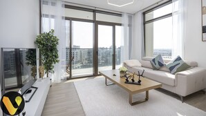 A modern living room with a sofa, coffee table, and a large window offering a city view. - Palace Waterfront Living Dubai Creek  (Dubai)