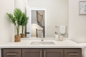 Ein Badezimmer mit Waschbecken, Holzschränken, einem Spiegel und einer Topfpflanze.