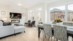 Un salon moderne doté d’un téléviseur à écran plat, d’une cheminée, d’un coin repas avec des chaises à motifs zébrés et d’une grande fenêtre donnant sur le quartier.