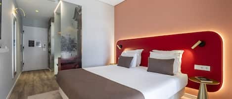 A modern hotel room with a large bed, a red accent wall, and a small bedside table.