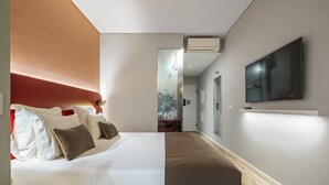 A modern hotel room with a large bed, a flat-screen TV mounted on the wall, and a hallway leading to other rooms. - King David Suites 501 by Homie (Funchal)