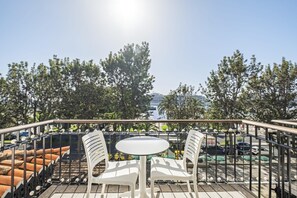 A terrace with a table and chairs, overlooking a parking area and a body of water with buildings in the distance. - King David Suites 401 by Homie (Funchal)