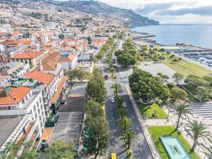 Un paysage urbain côtier avec une large rue bordée d’immeubles, une plage et une vue dégagée sur la mer.
