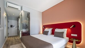 Ein modernes Hotelzimmer mit einem großen Bett, einer roten Akzentwand und einem kleinen Nachttisch.