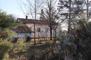 Une maison avec un toit en tuiles, entourée d’une végétation luxuriante et d’arbres.