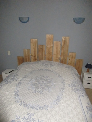 Une chambre à coucher avec une tête de lit en bois, une couvre-lit à motifs floraux et une table de chevet avec une lampe.