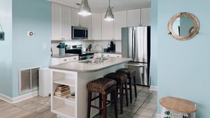 A modern kitchen with white cabinets, a central island with stools, stainless steel appliances, and pendant lighting. - New "Sandy Feet Retreat" 3bed Villa Capriani (North Topsail Beach)