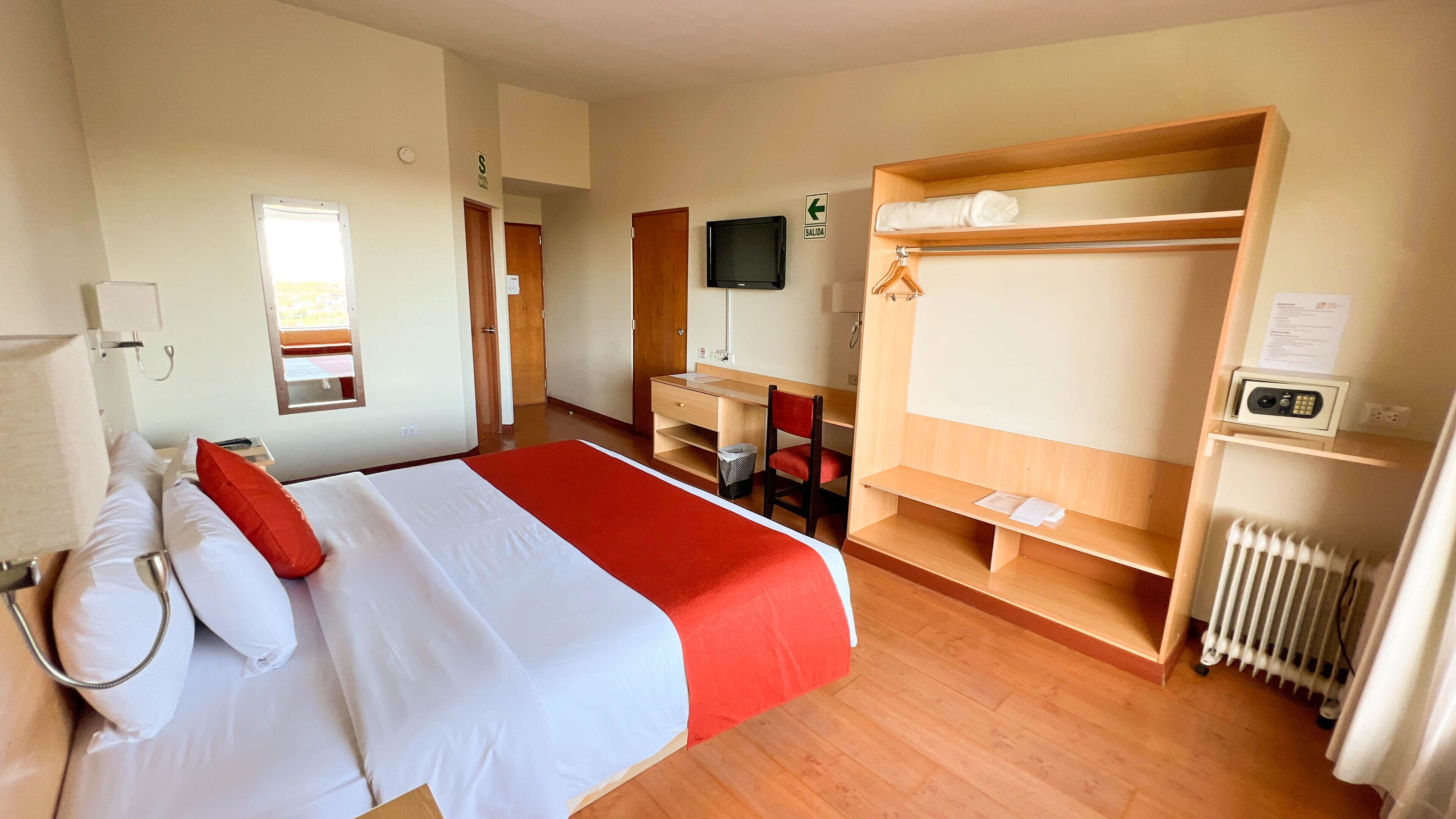 Habitación de hotel con cama, escritorio, silla, televisor y armario.