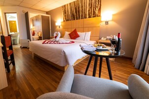 Habitación de hotel con una cama, una mesita de noche con una botella de vino, una silla y una pequeña mesa con comida.
