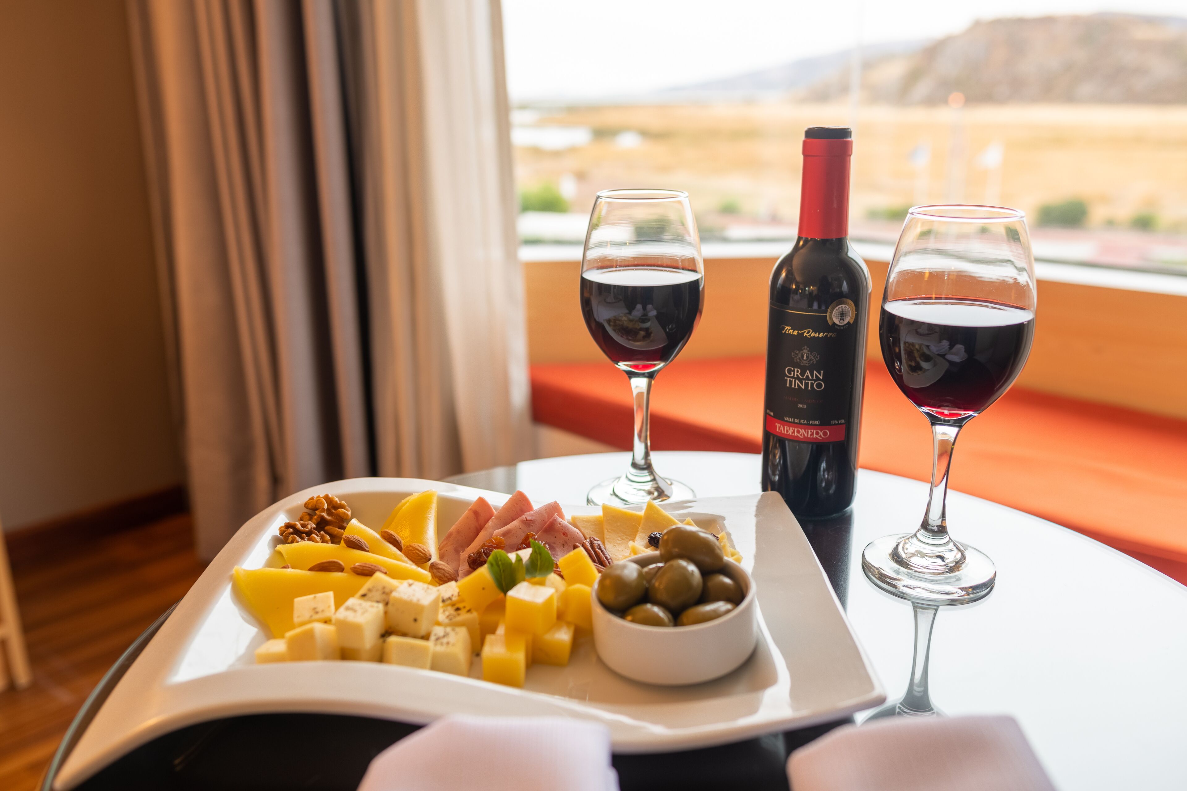A table with a cheese platter, two glasses of red wine, and a bottle of wine.