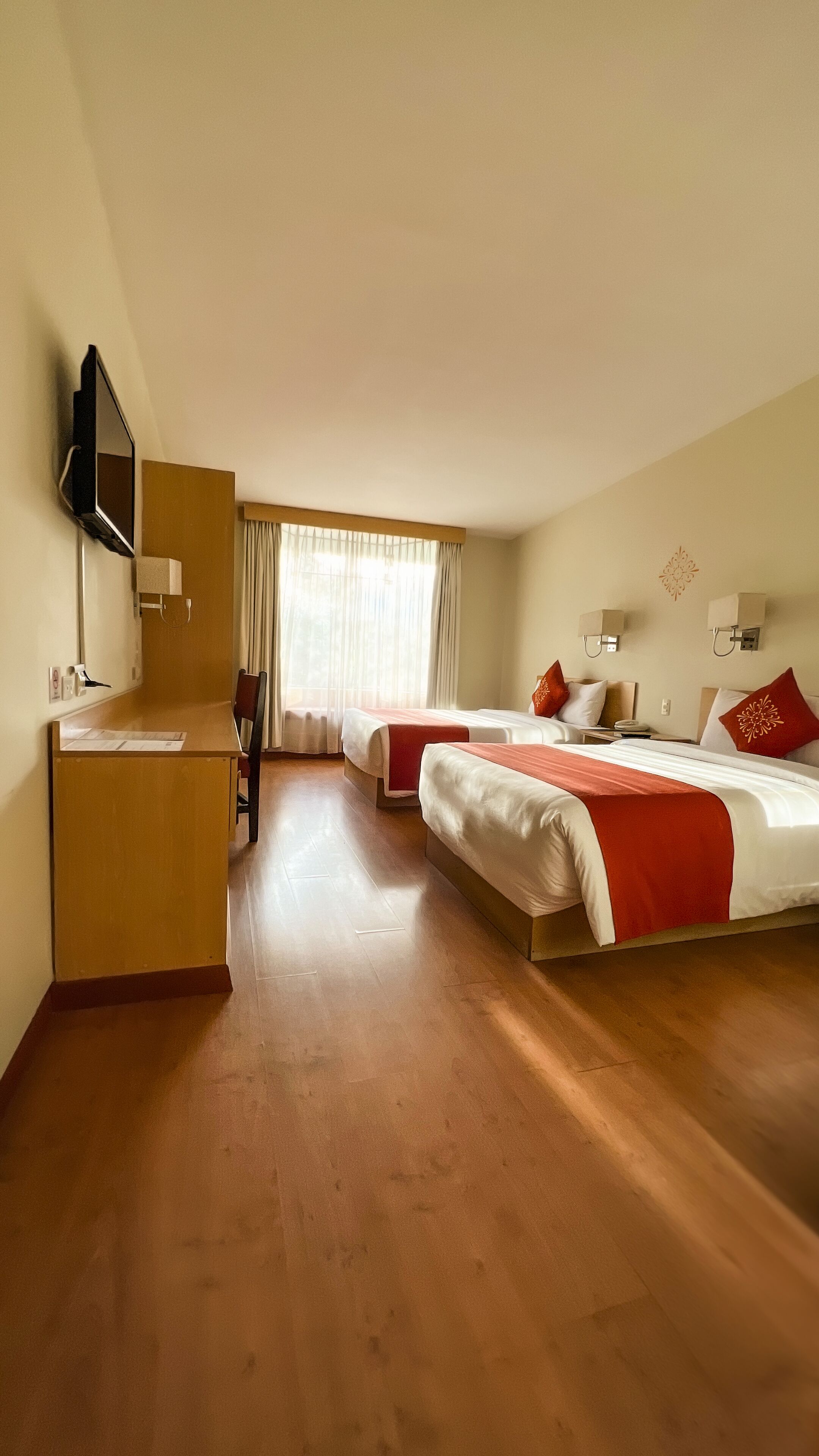 A hotel room with two beds, a desk, a chair, a TV, and a window with curtains.