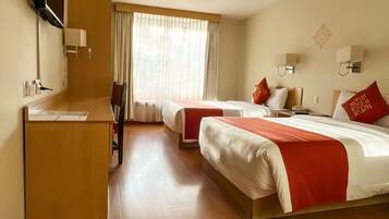 A hotel room with two beds, a desk, a chair, a TV, and a window with curtains.