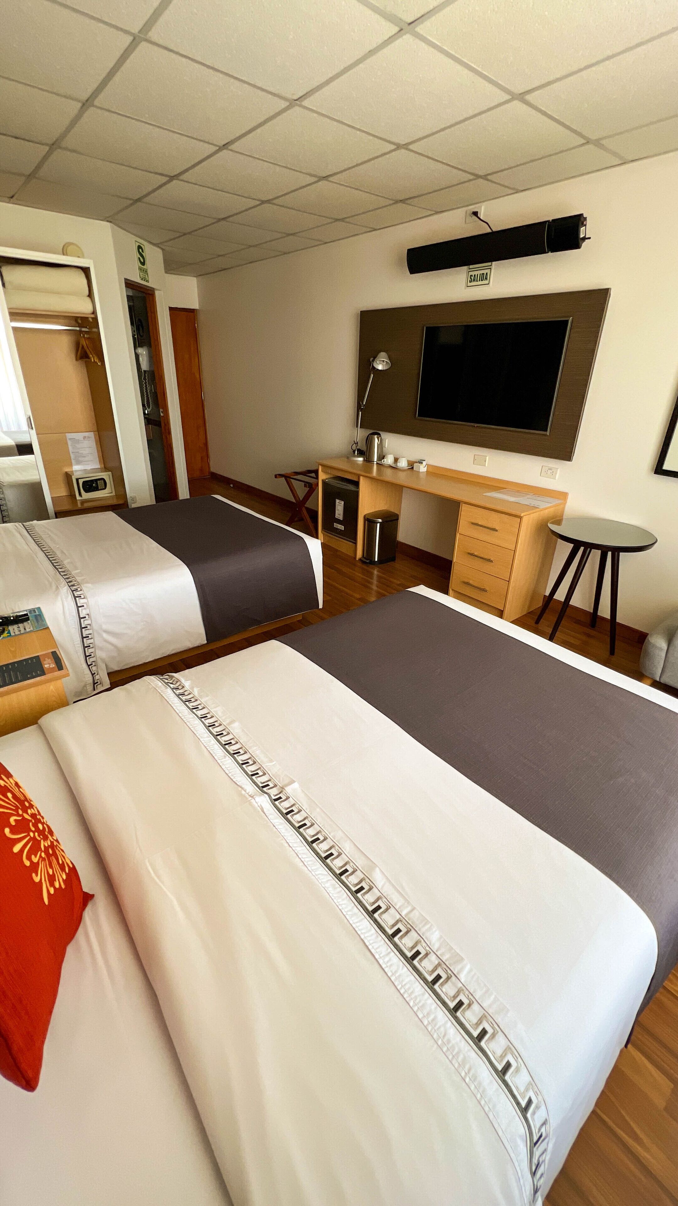 Une chambre d’hôtel avec deux lits, un bureau, une chaise, une télévision et une petite table.