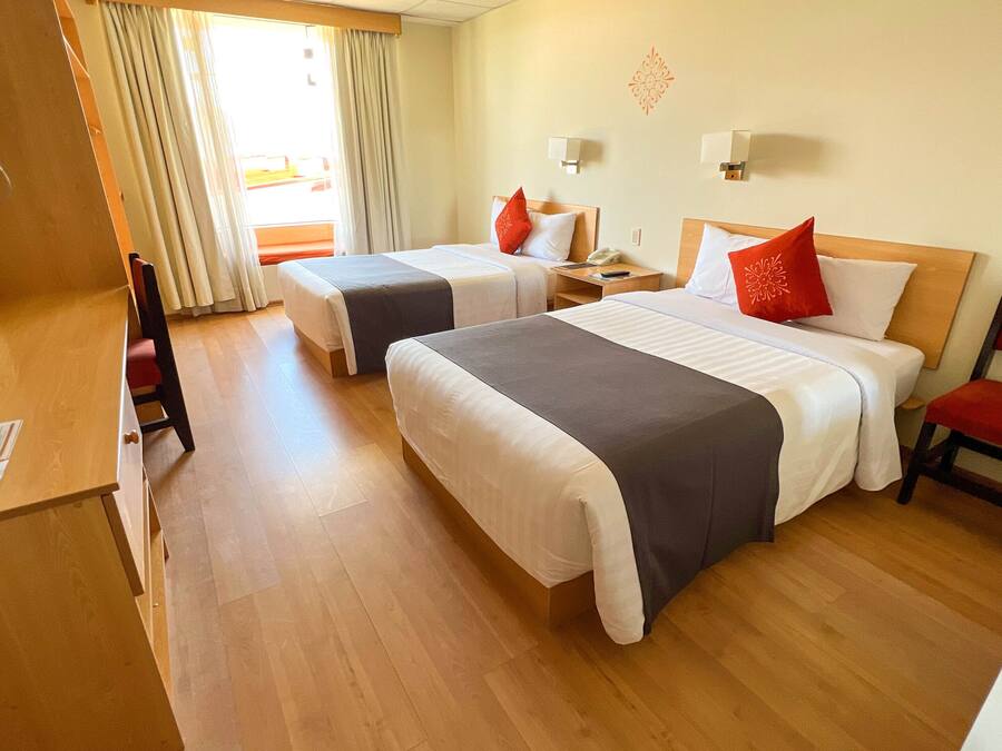 Habitación de hotel con dos camas, un escritorio, una silla y una ventana con cortinas.
