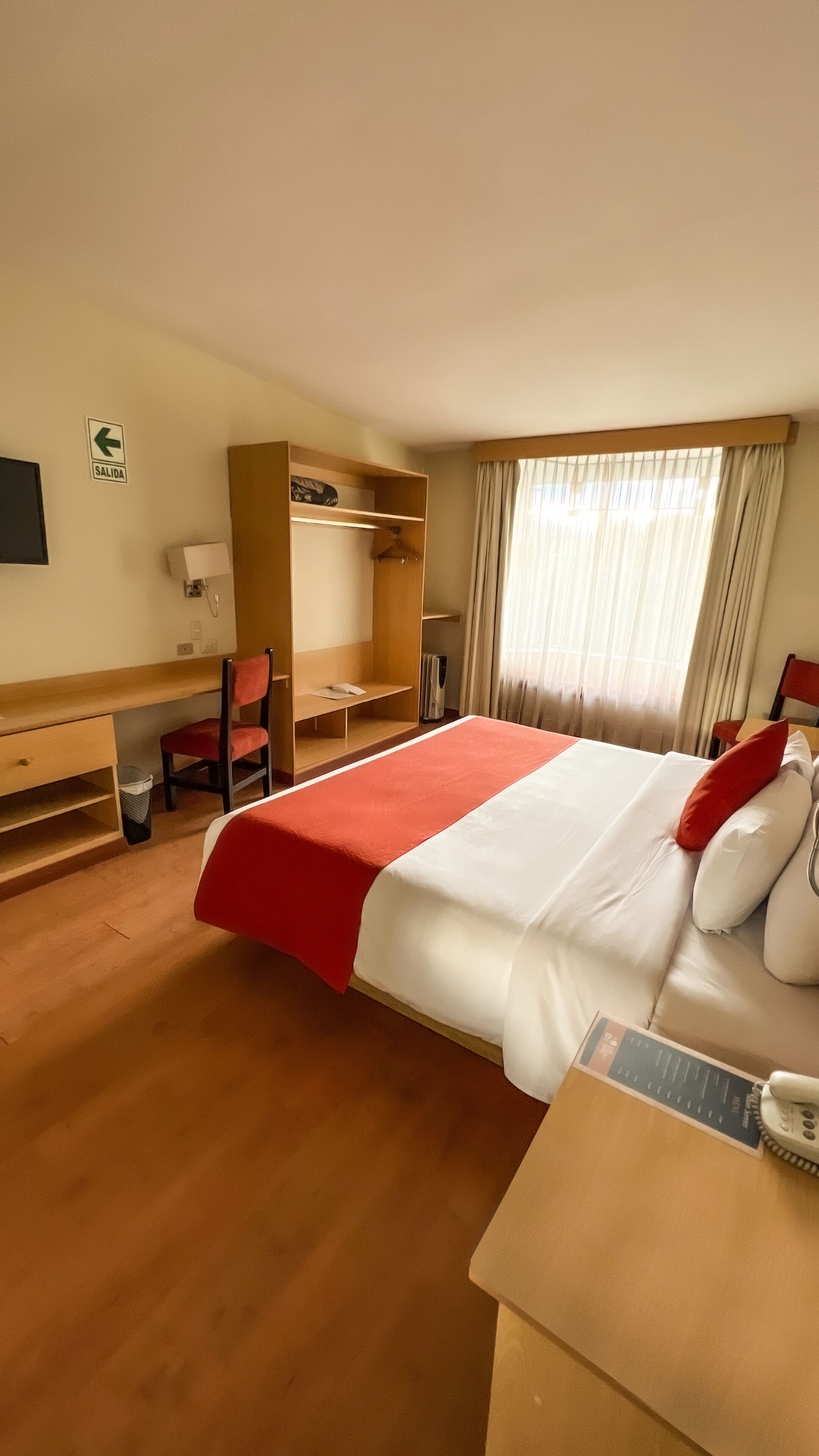 Una habitación de hotel con una cama grande, un escritorio, una silla, un armario y un televisor.