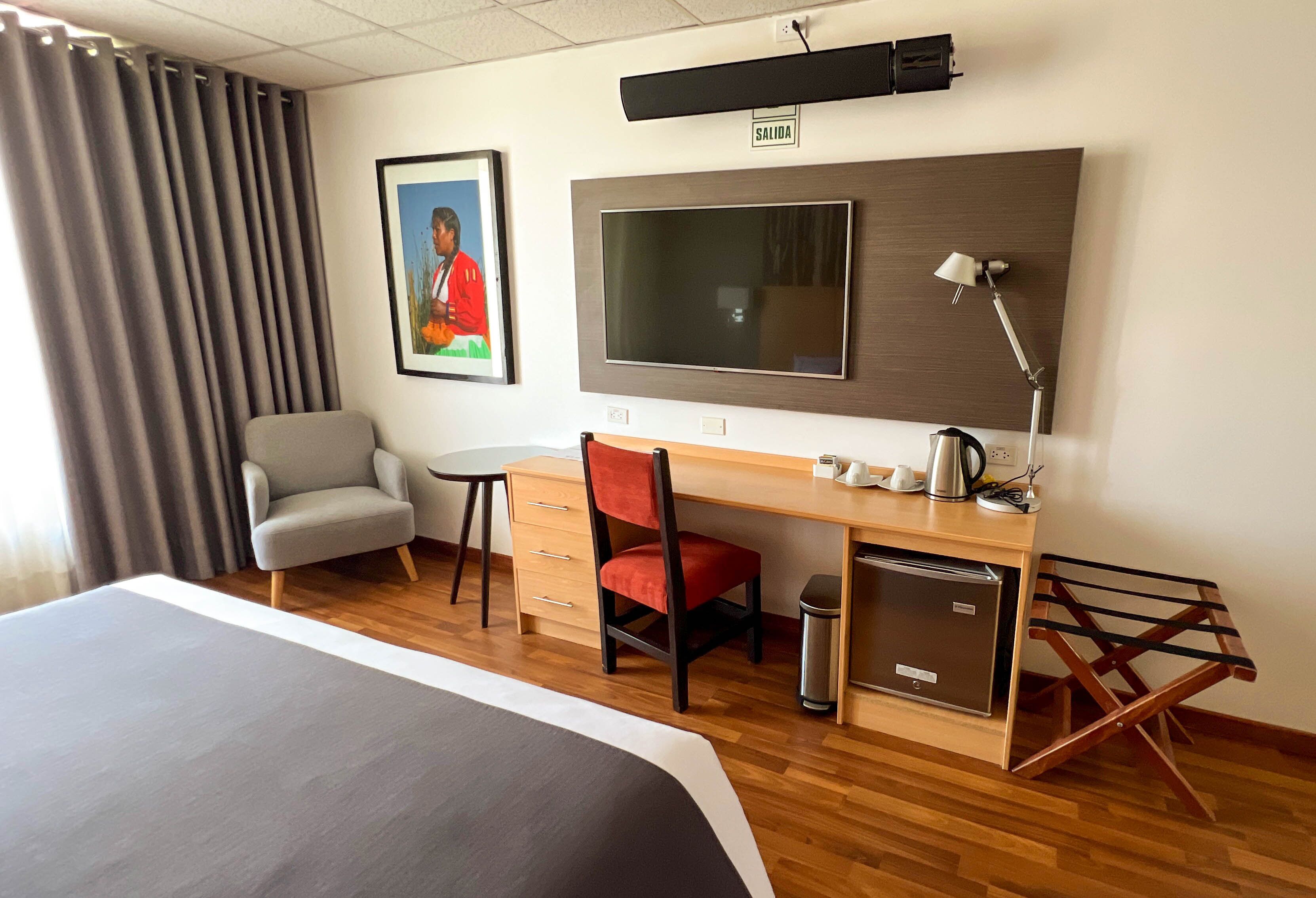 Une chambre d’hôtel comprenant un lit, un bureau avec une chaise, une télévision, une lampe et un petit réfrigérateur.