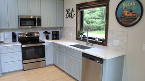 A modern kitchen with light blue cabinets, stainless steel appliances, and a large window offering a view of greenery. - Brand New Secluded Cabins in Arbor Vitae, WI (arbor vitae)