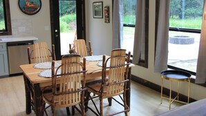 A dining area with a wooden table and chairs, a small side table, and a view of the outdoors through large windows. - Brand New Secluded Cabins in Arbor Vitae, WI (arbor vitae)