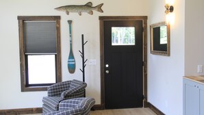 A room with a black door, a window with blinds, a fish decoration, a wall-mounted light, and a chair. - Brand New Secluded Cabins in Arbor Vitae, WI (arbor vitae)