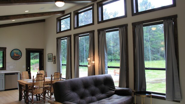 A spacious living room with a large window, a dining area with wooden chairs, and a sofa. - Brand New Secluded Cabins in Arbor Vitae, WI (arbor vitae)