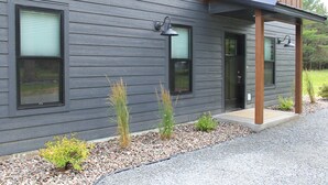 A modern building with a grey exterior, two windows with black frames, and a wooden porch with a black railing. - Brand New Secluded Cabins in Arbor Vitae, WI (arbor vitae)
