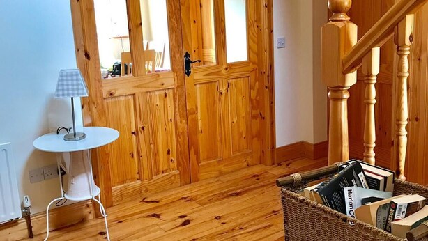 A wooden-floored room with a white table, a wicker basket, and a wooden staircase. - 2 min's to beautiful beach, amazing home for 8 peeps huge garden. Suits families (Portsalon)