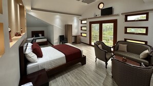 Une chambre spacieuse avec un grand lit, un coin salon avec un canapé et des fauteuils, et un balcon doté de grandes fenêtres.