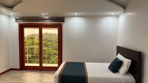Une chambre à coucher avec un lit, une tête de lit en bois et une vue sur un balcon, accessible par une porte vitrée.