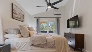 A bedroom with a bed, a ceiling fan, a TV, and a window with curtains. - The River Nest-Hot Tub & River View (Fountain Lake)