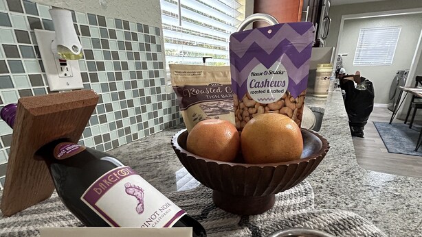 Una encimera de cocina con una botella de vino, un cuenco de anacardos y un cuenco de galletas con forma de corazón.
