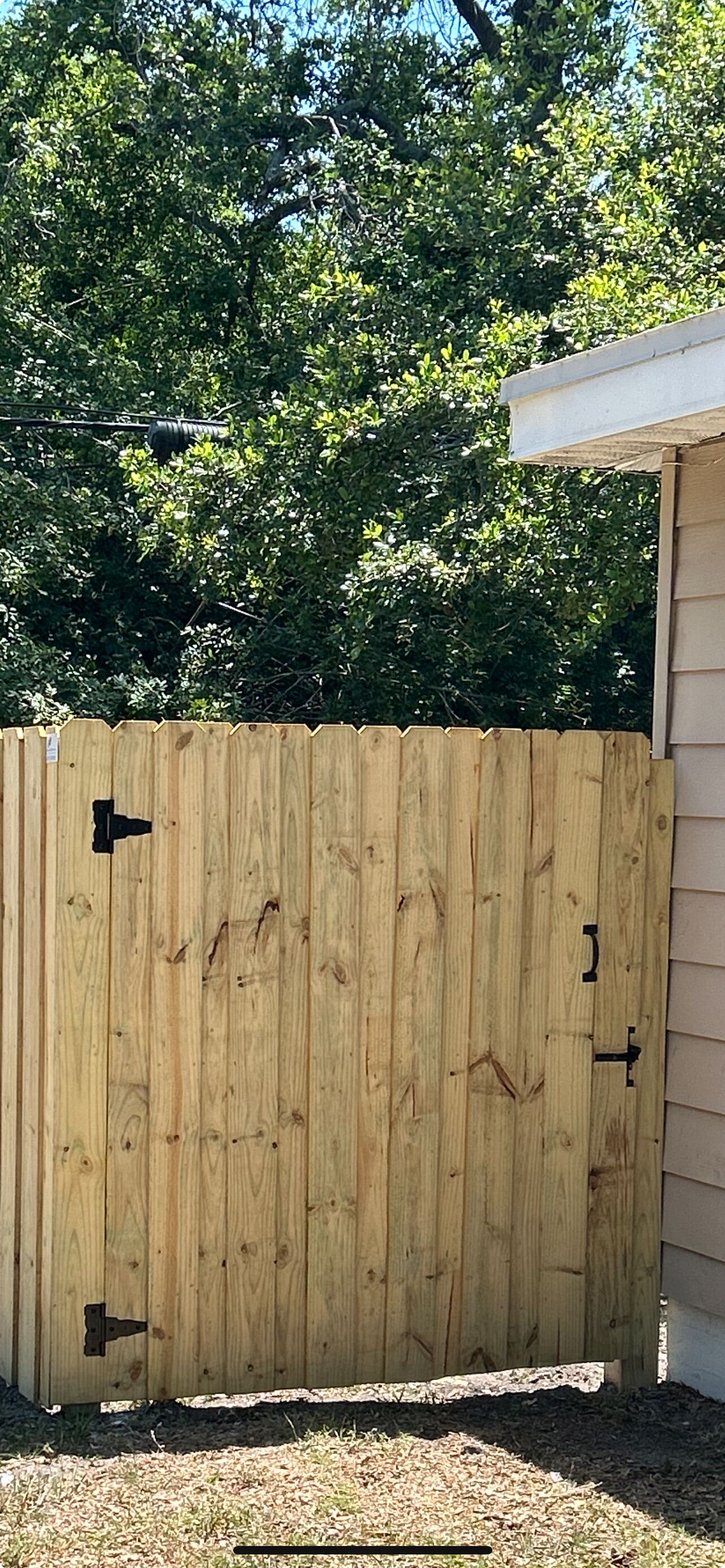 A wooden fence with metal hinges and a latch, a grassy area, and a building with siding in the background.