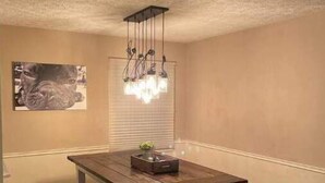A dining area with a wooden table and benches, a hanging light fixture, and a framed picture on the wall. - Three Kings Ranch (Indianapolis)