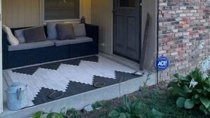 A covered porch with a sofa, wall-mounted lights, and a brick wall. - Three Kings Ranch (Indianapolis)